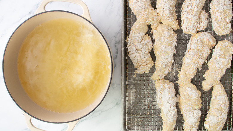 Pot of oil next to rack of raw and coated chicken tenders