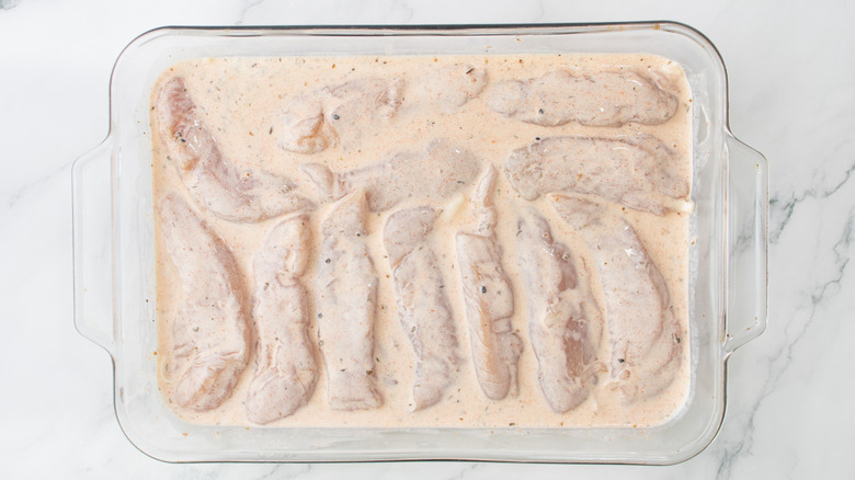chicken strips soaking in seasoned buttermilk in casserole dish