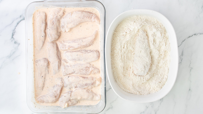 dredging chicken strip in dry mixture next to marinated chicken strips in casserole dish