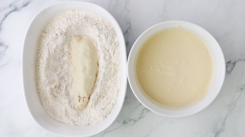 chicken tender coated in wet batter in dry mixture next to bowl of wet batter