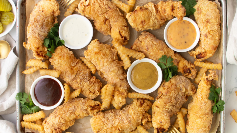 baking sheet covered with crispy chicken tenders, fries, and dips
