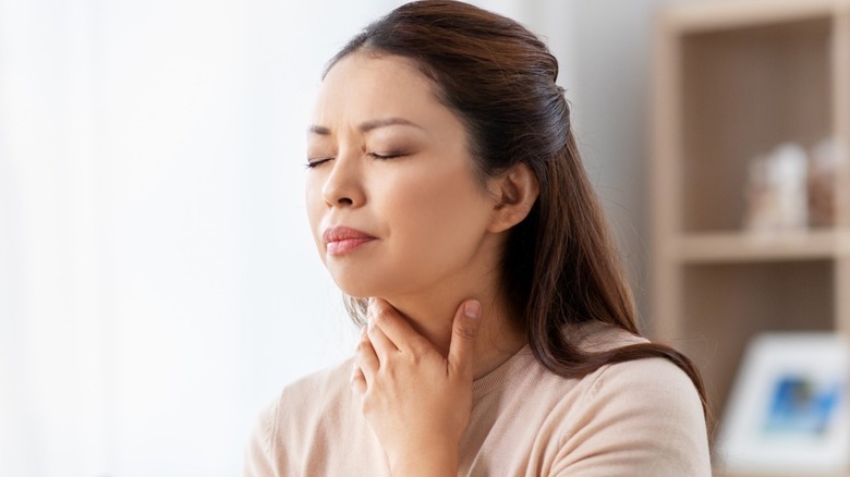 Woman grabbing throat with eyes closed