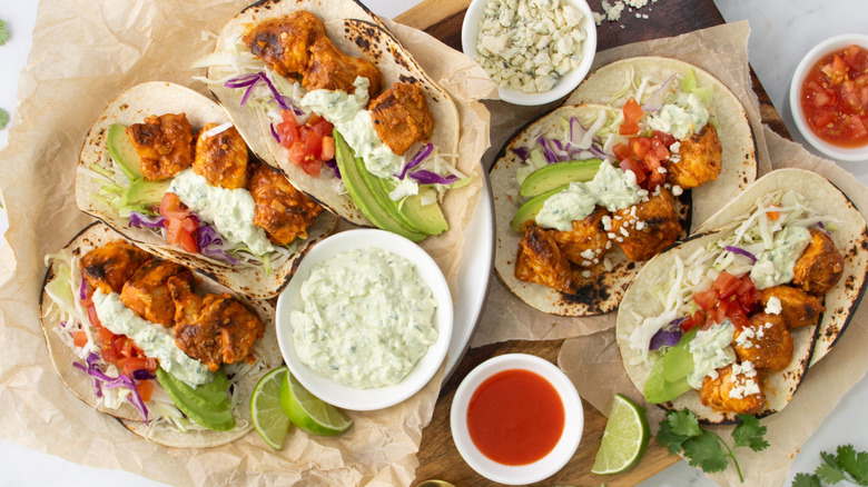 Buffalo chicken tacos next to bowls of sauces and blue cheese