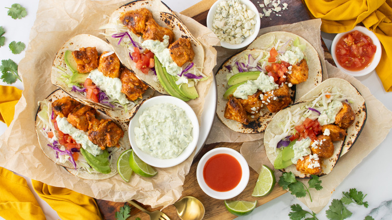 Buffalo chicken tacos next to bowls of sauces and blue cheese