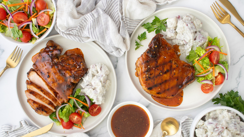 two plates with grilled pork chops, bbq sauce, and salad