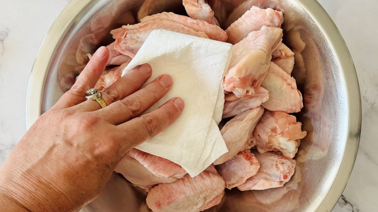 Hand patting chicken wings dry with paper towel