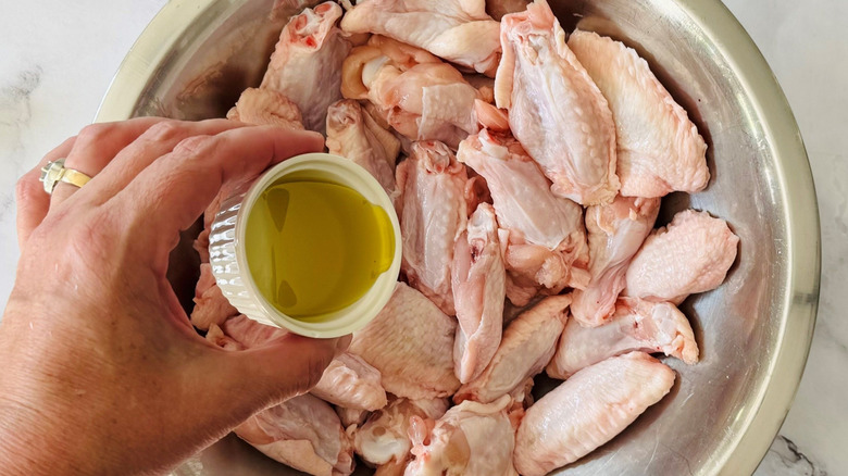 Hand pouring small bowl of oil over chicken wings
