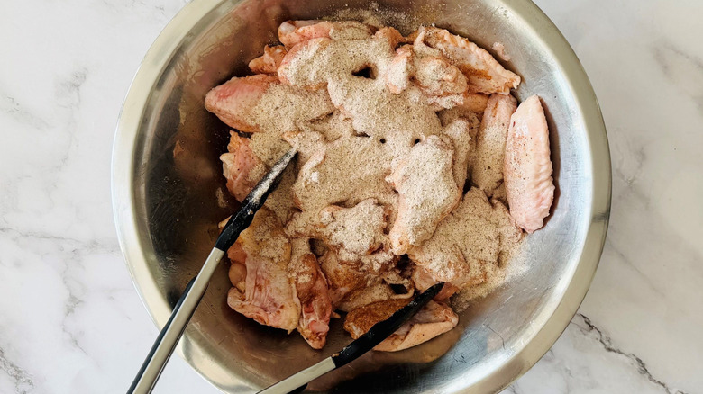 Tongs in bowl with chicken wings coated in dry rub