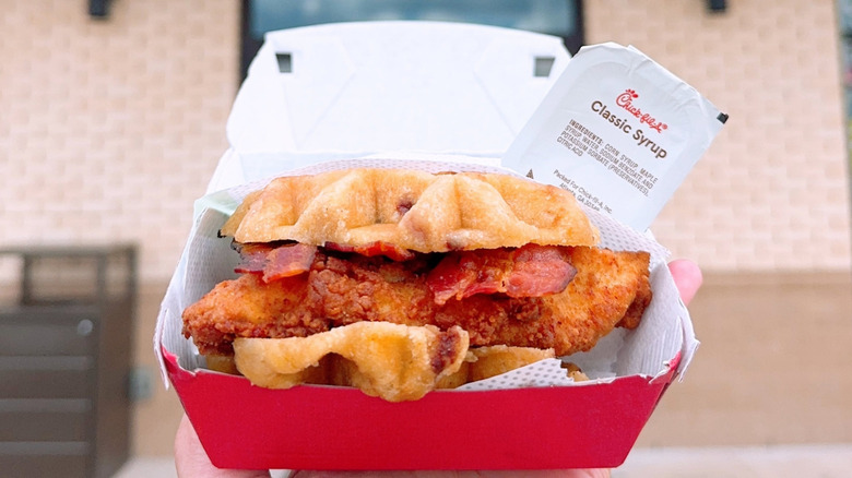 A Chick-fil-A Chicken & Waffles Sandwich in a to-go container with a packet of Classic Syrup