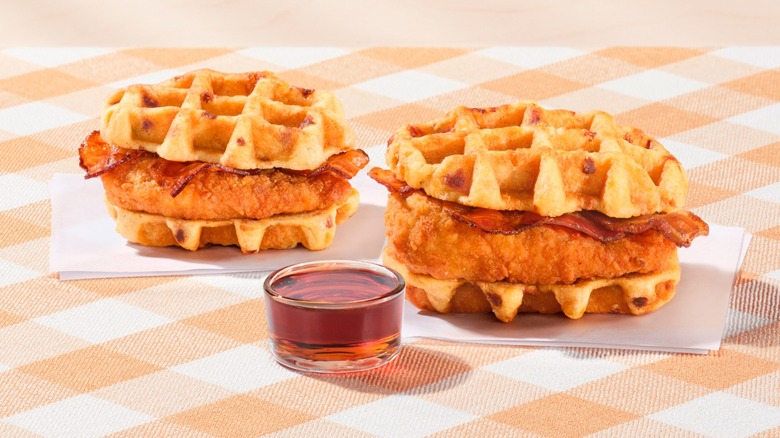 Two Chick-fil-A Chicken & Waffle Sandwiches with a container of maple syrup.