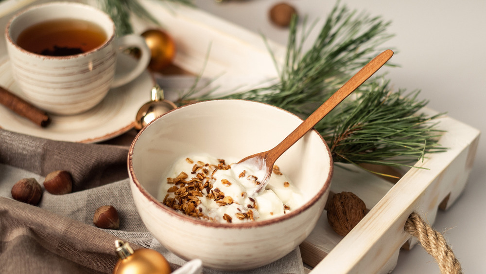 Bowl of Greek yogurt with granola on tray with tea, nuts, spices, and holiday décor