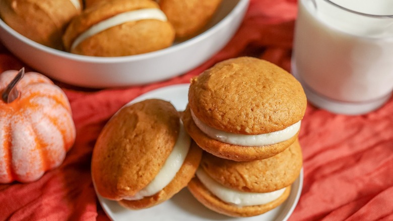 Pumpkin whoopie pies on plate with more and glass of milk in background
