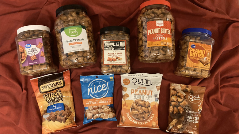 Jars of peanut butter pretzels from various brands on red tablecloth.