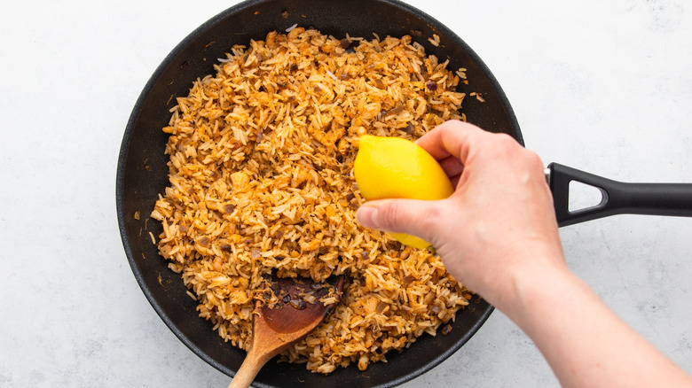 Squeezing lemon juice into pan of rice and seafood