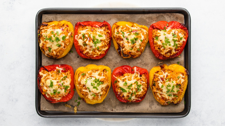 Cheesy stuffed bell peppers with parsley garnish, on parchment-lined baking sheet