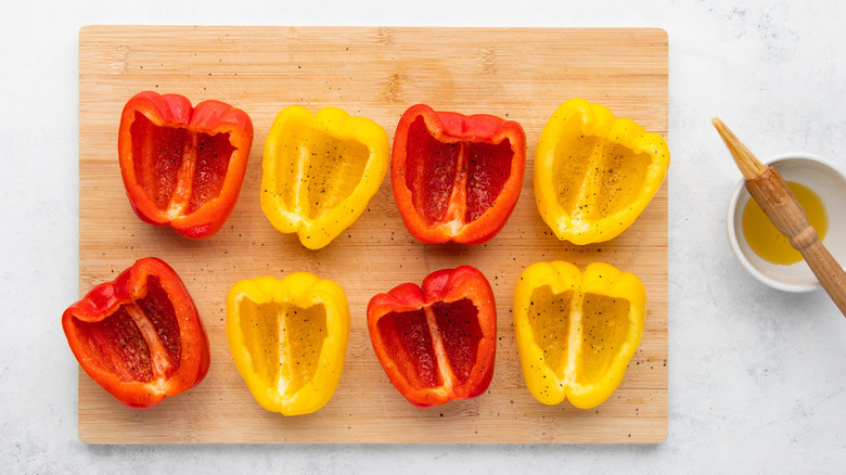 Halved bell peppers on wooden cutting board next to small bowl of olive oil