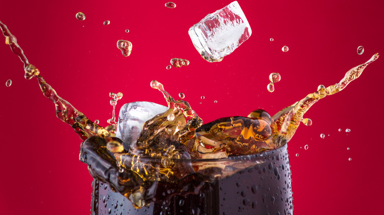 Glass of Coca-Cola with ice splashing out against red background