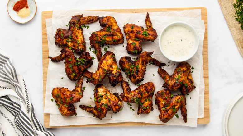 Barbecue chicken wings on cutting board with bowl of ranch dip