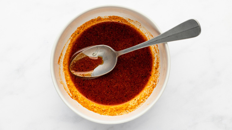 Mixture of oil and spices in a bowl with metal spoon