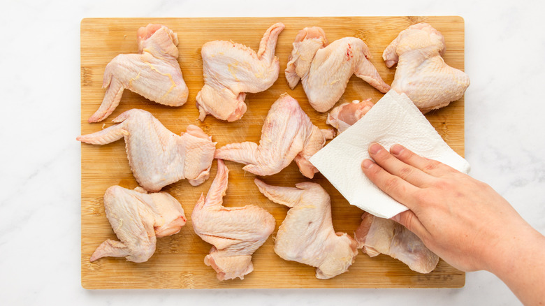 Chicken wings on cutting board being patted dry with paper towel