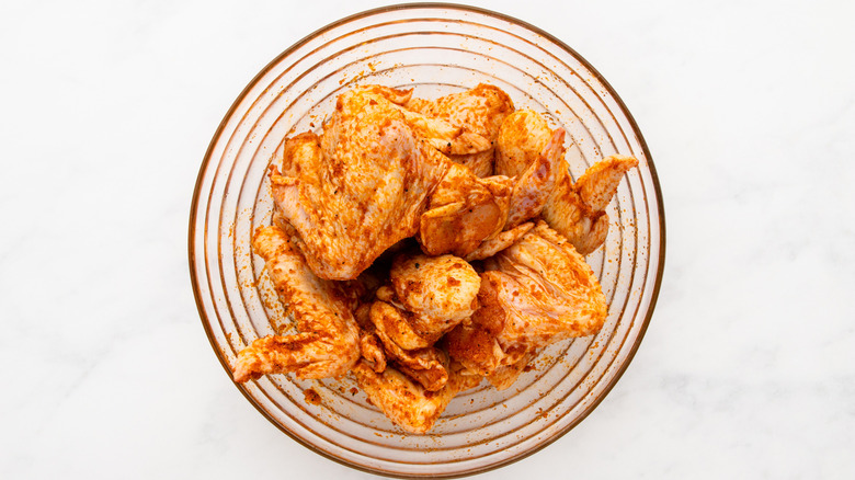 Bowl of spice-coated chicken wings on marble surface