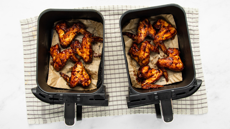 Half-cooked chicken wings in two air fryer baskets on top of cloth