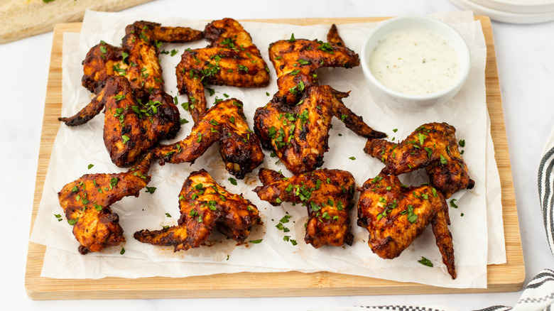 BBQ chicken wings on parchment-lined cutting board with bowl of ranch sauce