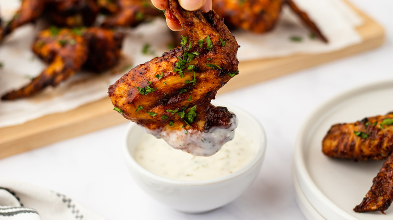 Hand dipping barbecue chicken wing into bowl of ranch sauce