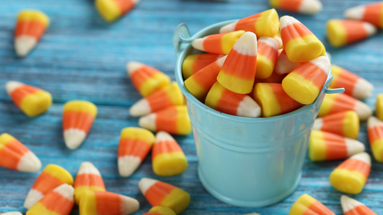 A small blue pail of candy corn on a blue table top 