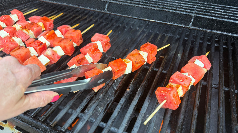 Tongs flipping watermelon and halloumi skewer on grill