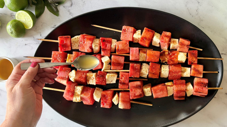 Spoon drizzling sauce over watermelon and halloumi skewers