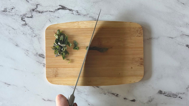 Knife cutting mint on wooden board