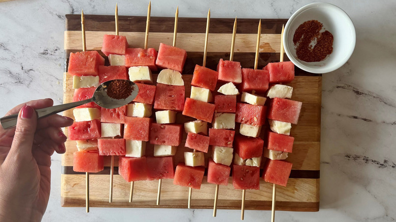 Sprinkling tajin mixture onto watermelon and halloumi skewers