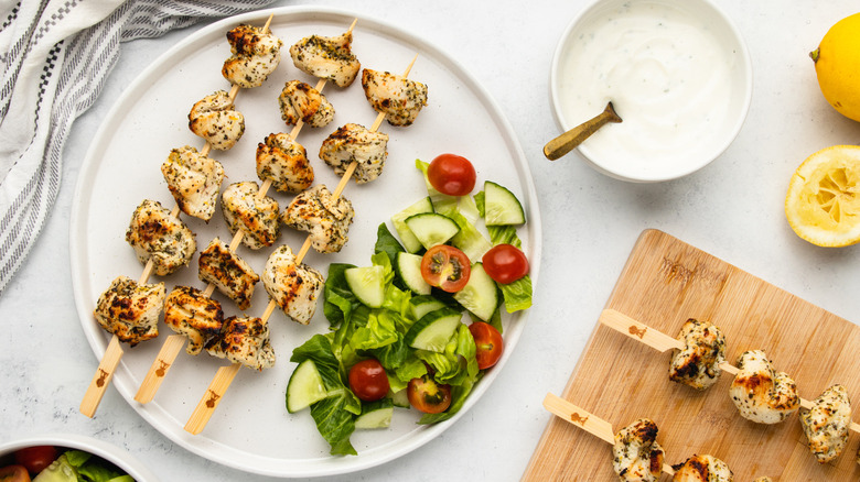 Chicken skewers on plate with side salad, next to bowl of creamy garlic dip