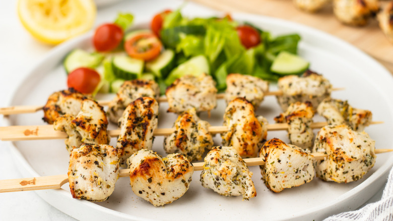 Lemon-herb chicken skewers on plate with side salad