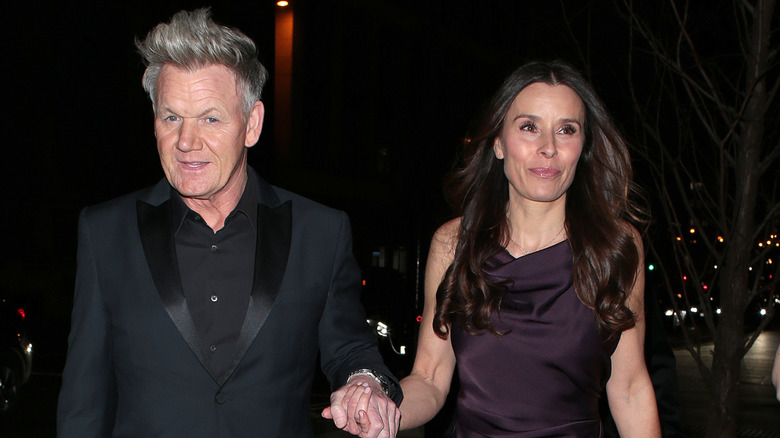 Gordon Ramsay and his wife Tana stand smiling hand in hand in formal attire on rooftop at nighttime