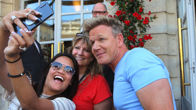 Gordon Ramsay taking a selfie with fans in front of building entrance