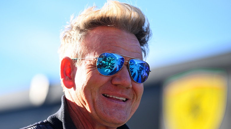 Gordon Ramsay's face in focus smiling and wearing reflective sunglasses