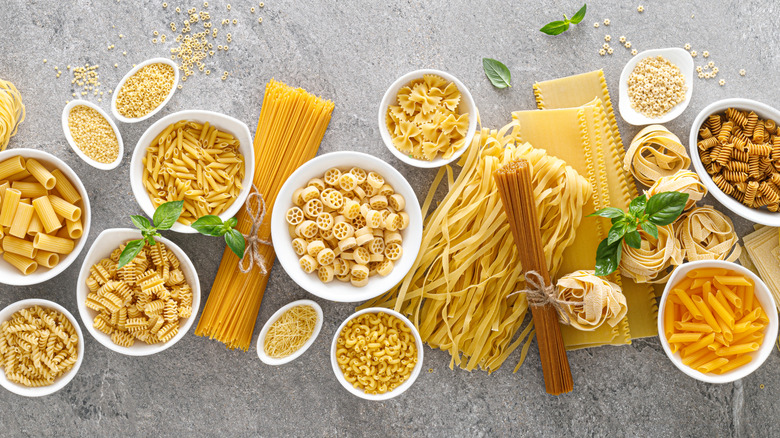 Various types of dried pasta in small white bowls and some in between