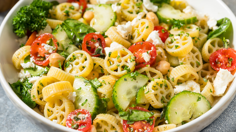 White bowl of pasta salad with wagon wheel pasta, various vegetables, and crumbled cheese