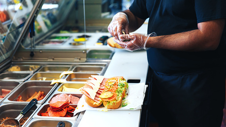 A man assembling a sandwich while wearing gloves