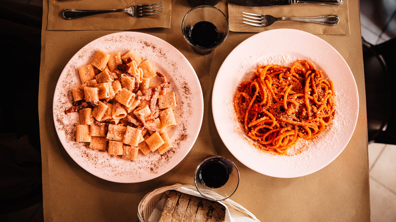 Two plates of pasta shown from overhead view with drinks and silverware nearby