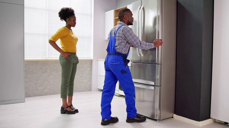 Man installing fridge while woman looks on