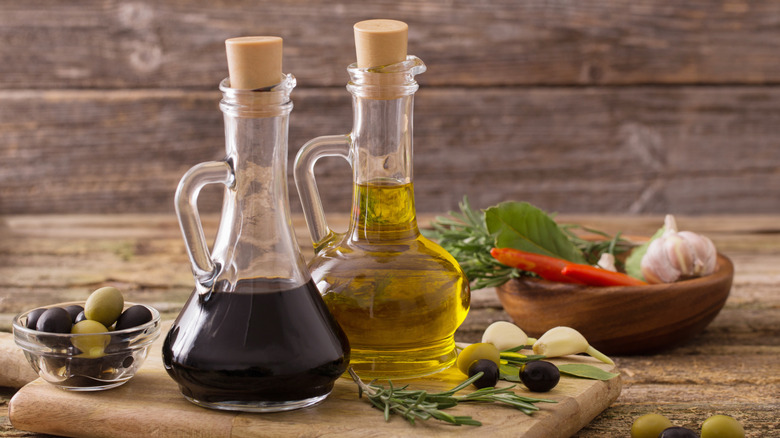 Oil and vinegar in glass bottle with cork on wooden cutting board