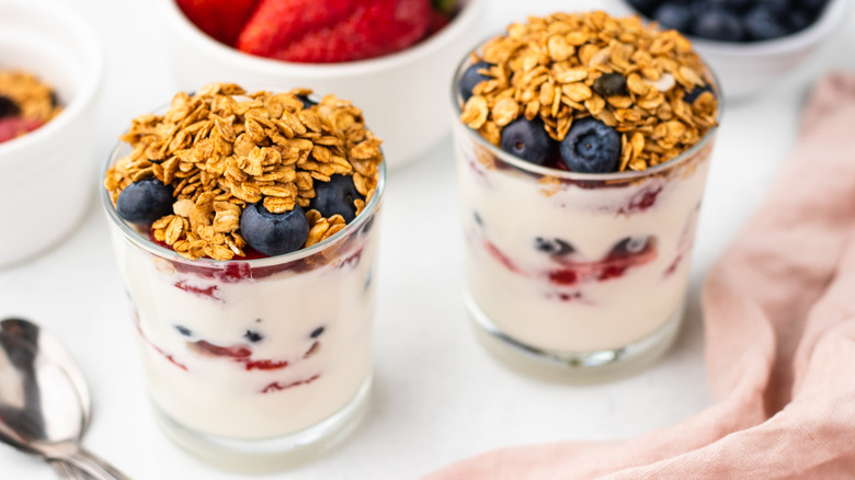Two breakfast parfaits in glasses, topped with blueberries and granola