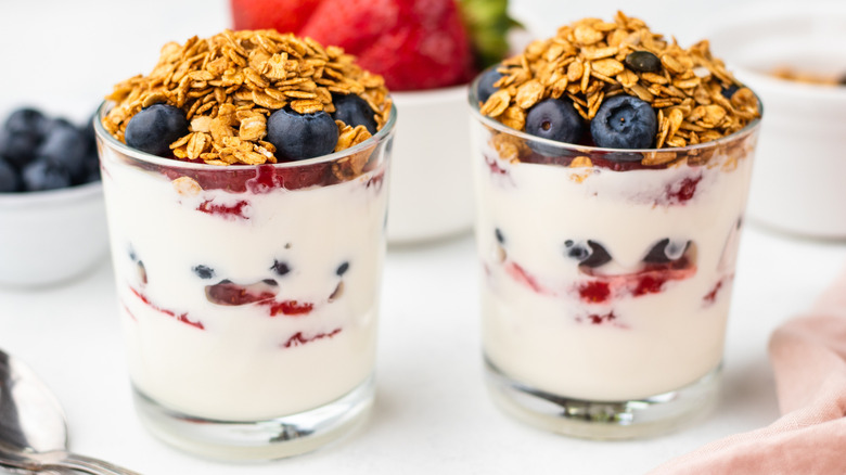 Two breakfast parfaits in glasses, topped with blueberries and granola