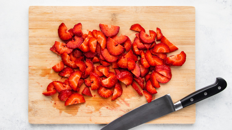 Sliced strawberries on wooden cutting board with knife