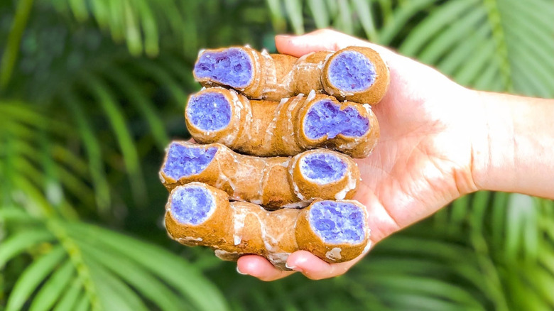 Hand holding two poi mochi donuts split in half.