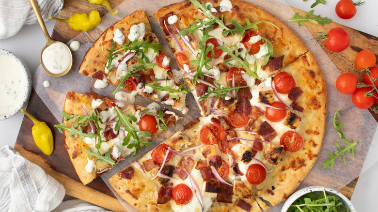Sliced chicken bacon ranch pizza with ranch and arugula