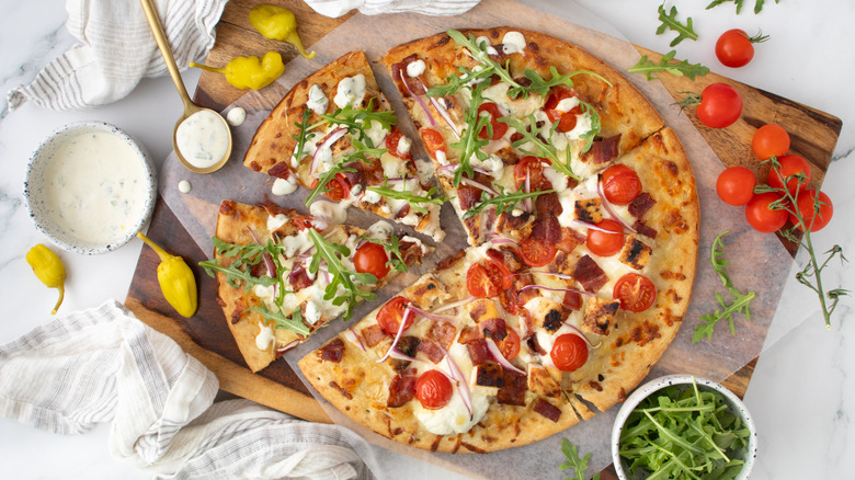 Chicken bacon ranch pizza cut into slices next to ranch sauce, arugula, and tomatoes